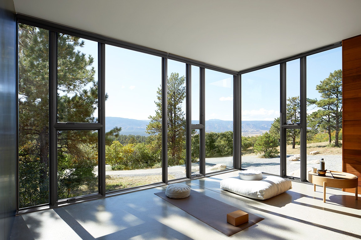 A serene meditation room with floor-to-ceiling windows overlooking trees and mountains, filled with natural light.