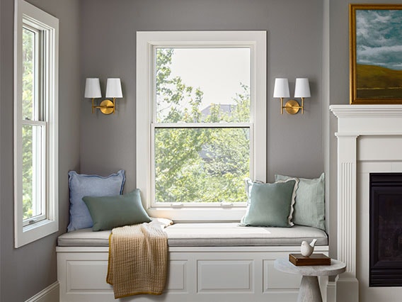 a single window over a window bench with blue-shaded pillows and a tan throw blanket