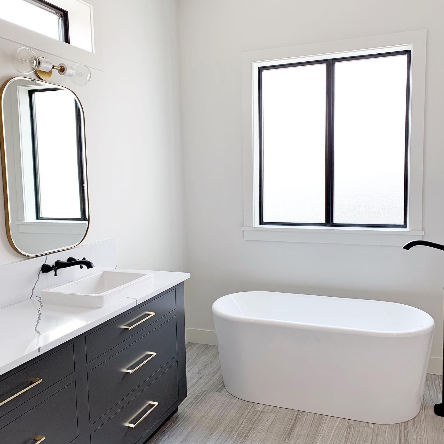 Black and white bathroom features white tub with black sliding window overhead