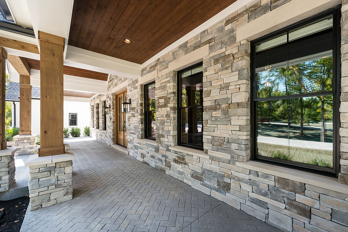Front porch with stone exterior walls, black-framed windows, wood ceiling, and herringbone paver floor.