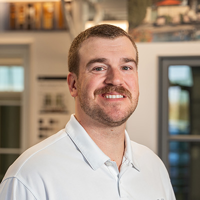 A man with short brown hair and a brown mustache is wearing a white Pella shirt.