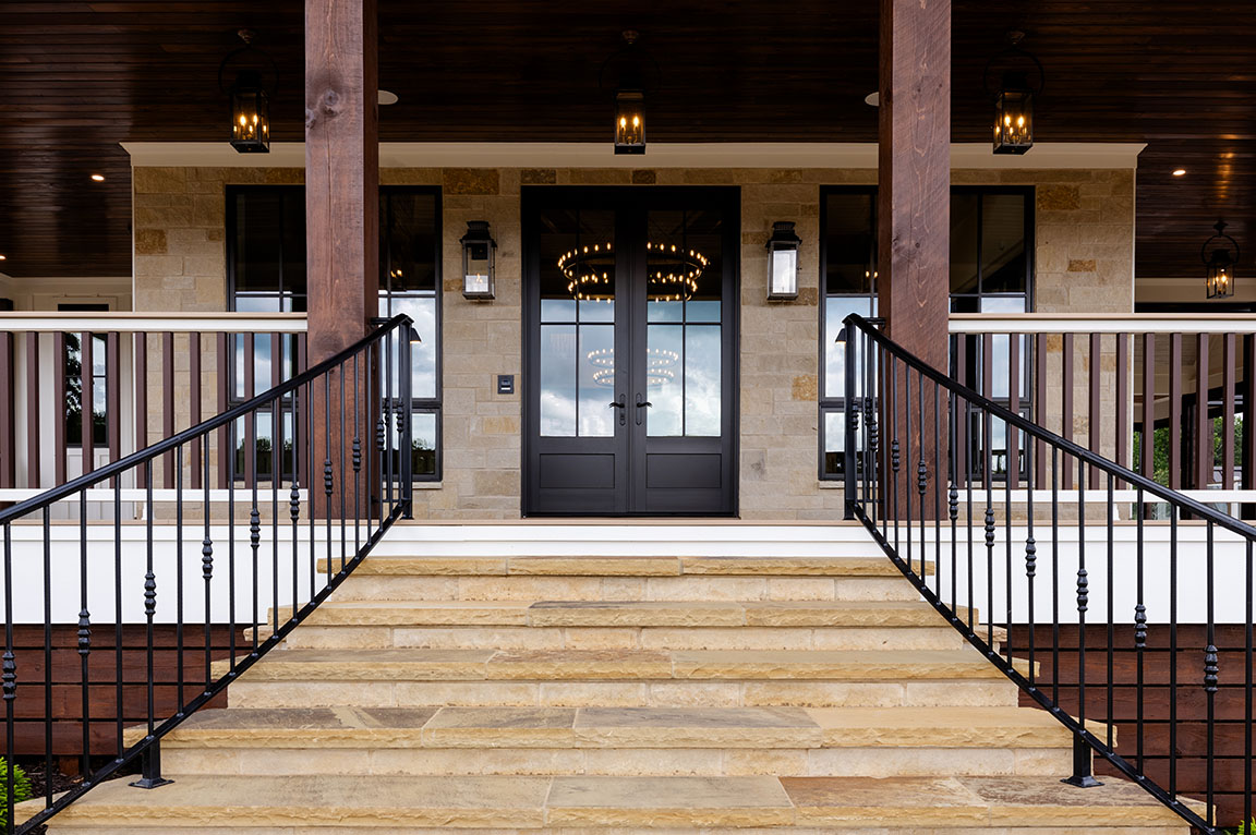 Elegant front porch with stone steps leading to a double door entrance, featuring black railings and outdoor lanterns.