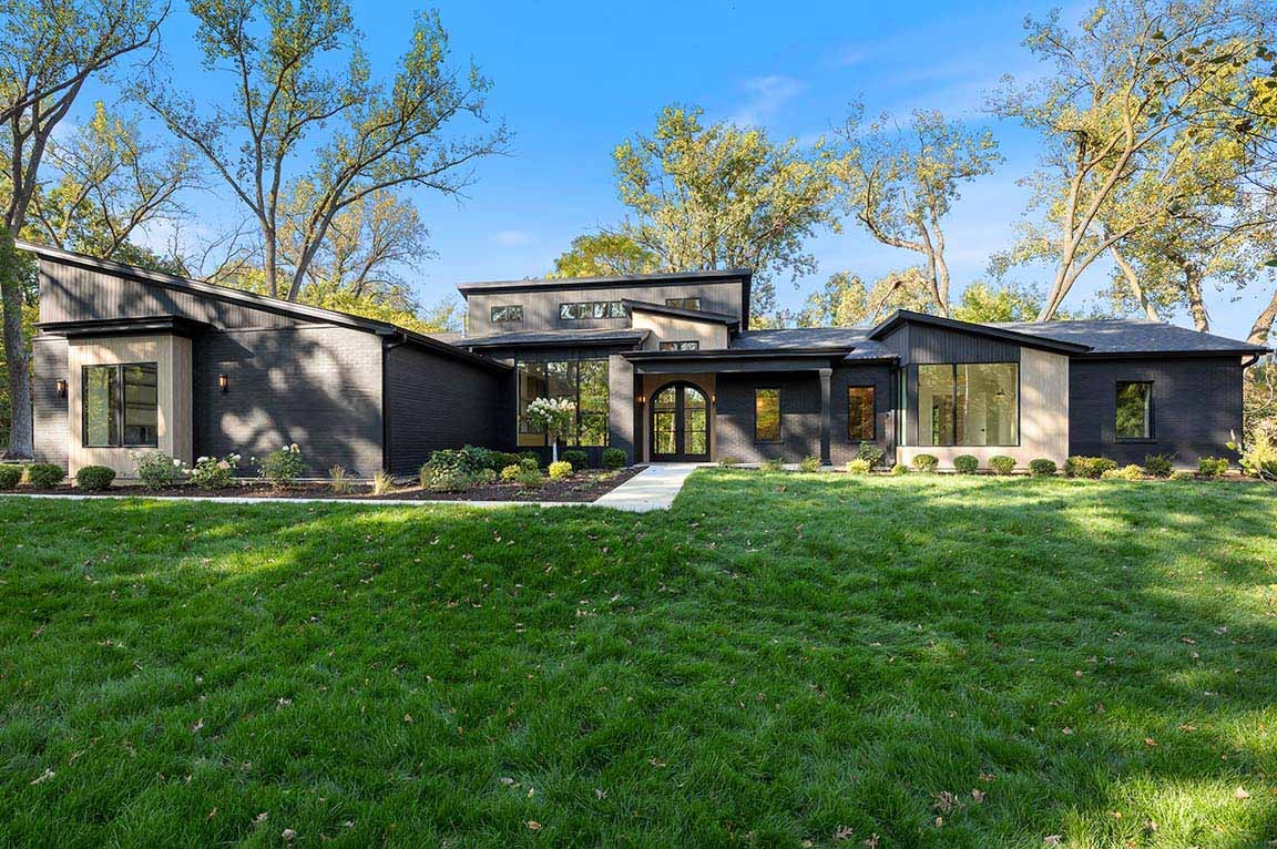 Wide view of modern black home exterior with expansive lawn, layered rooflines, and large windows.