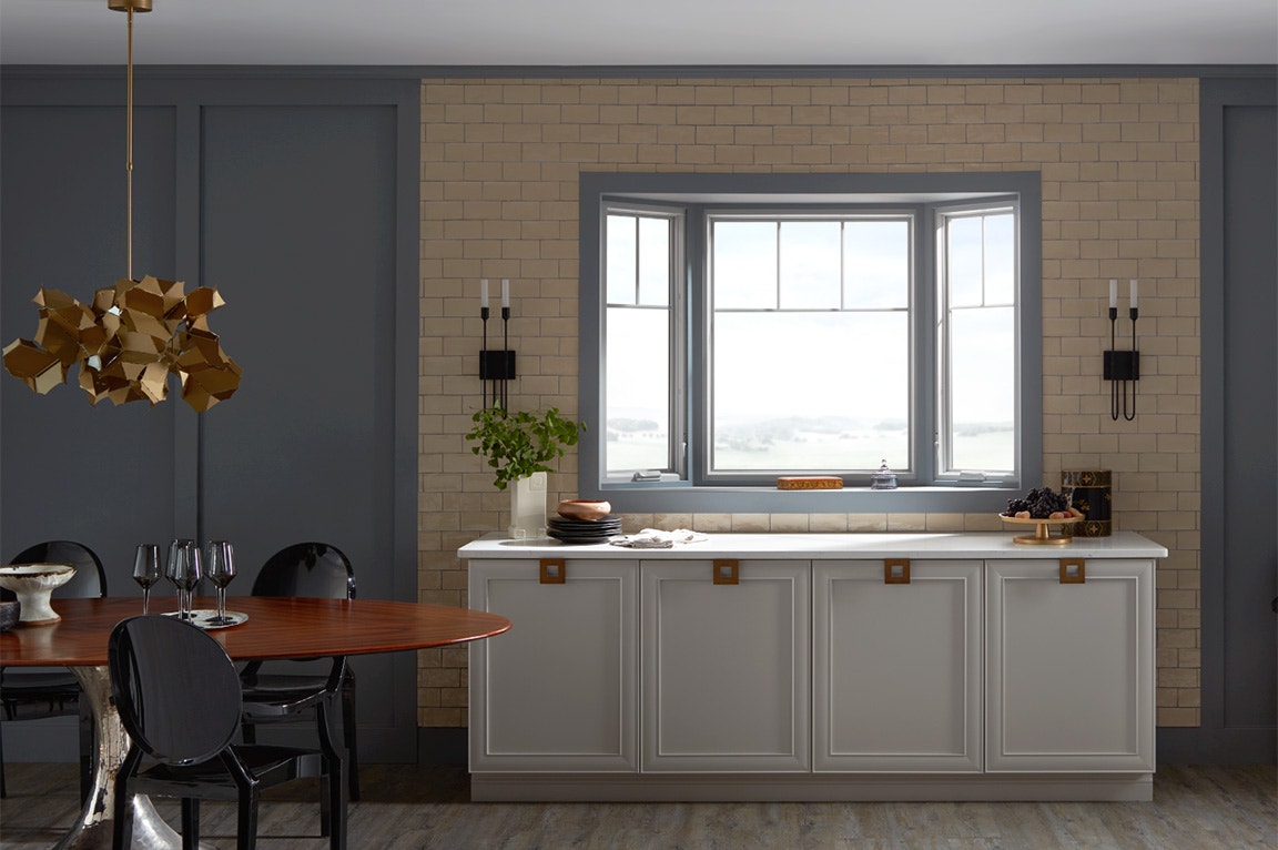 A modern kitchen featuring a bay window, gray cabinetry, and a wooden dining table.