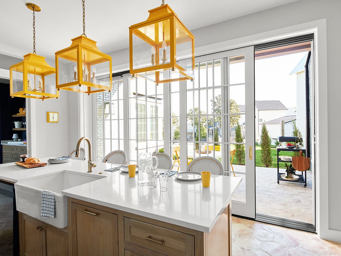 3 gold pendants hang over a kitchen island in front of a large white multi-slide patio door that has grilles between-the-glass.