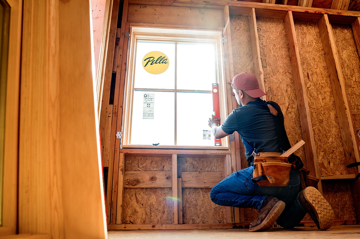 A man kneeling and using a level to install a replacement window in a wooden frame, demonstrating replacing a replacement window.