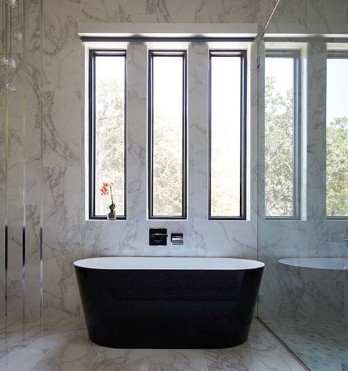 a contemporary soaker tub sits below three tall and narrow picture windows