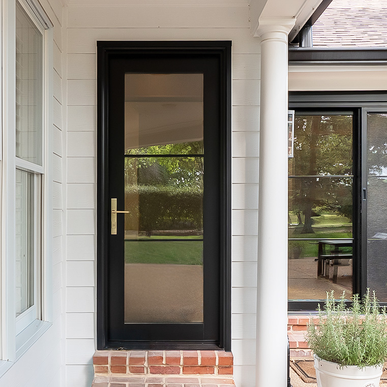 Modern black hinged entry door with full glass panel and brass handle on white siding exterior.