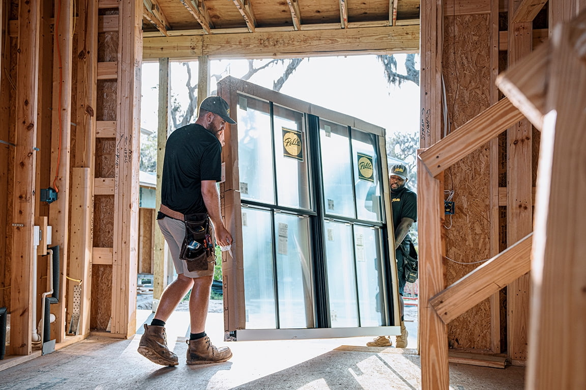 Two workers installing a large replacement window at a construction site, demonstrating replacing a replacement window.