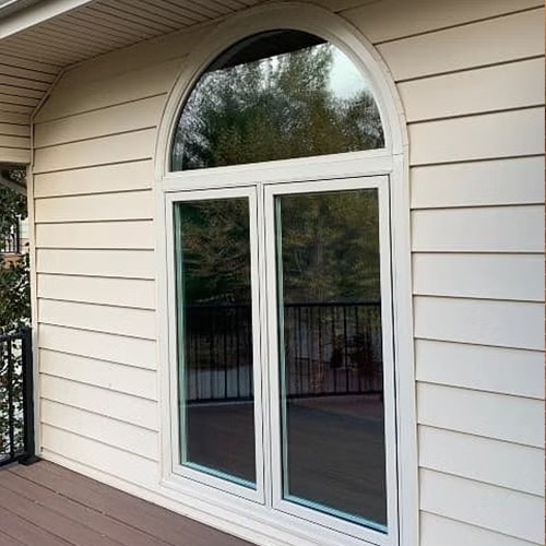 Two tan casement windows start at the floor of an exterior deck and have an arched unit spanning the windows.
