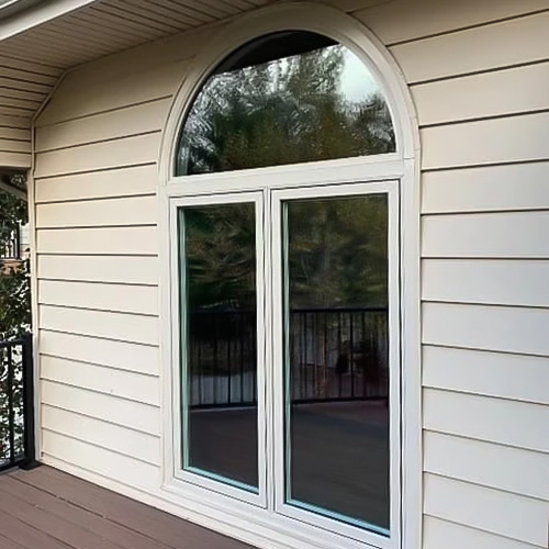 Two tan casement windows start at the floor of an exterior deck and have an arched unit spanning the windows.