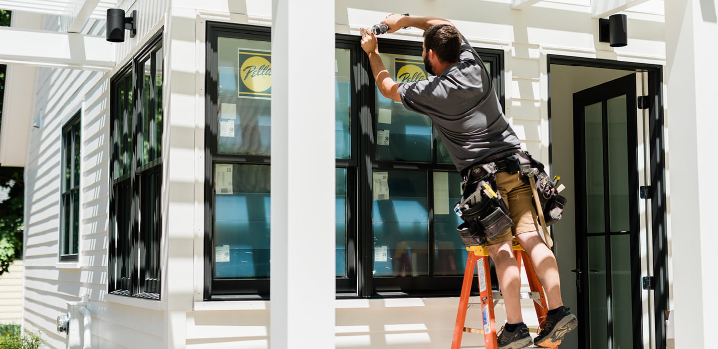 a construction worker on a ladder installing a black window