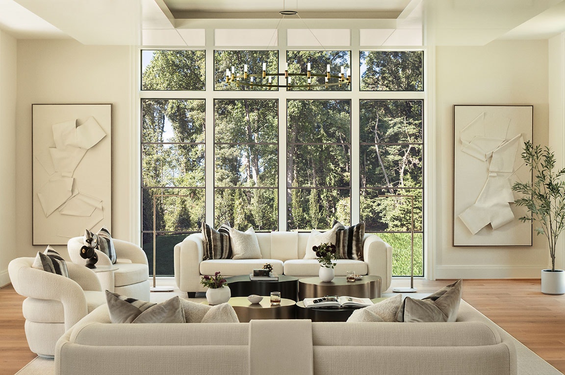 Spacious living room with floor-to-ceiling windows, neutral sofas, modern art, and a view of lush greenery outside.