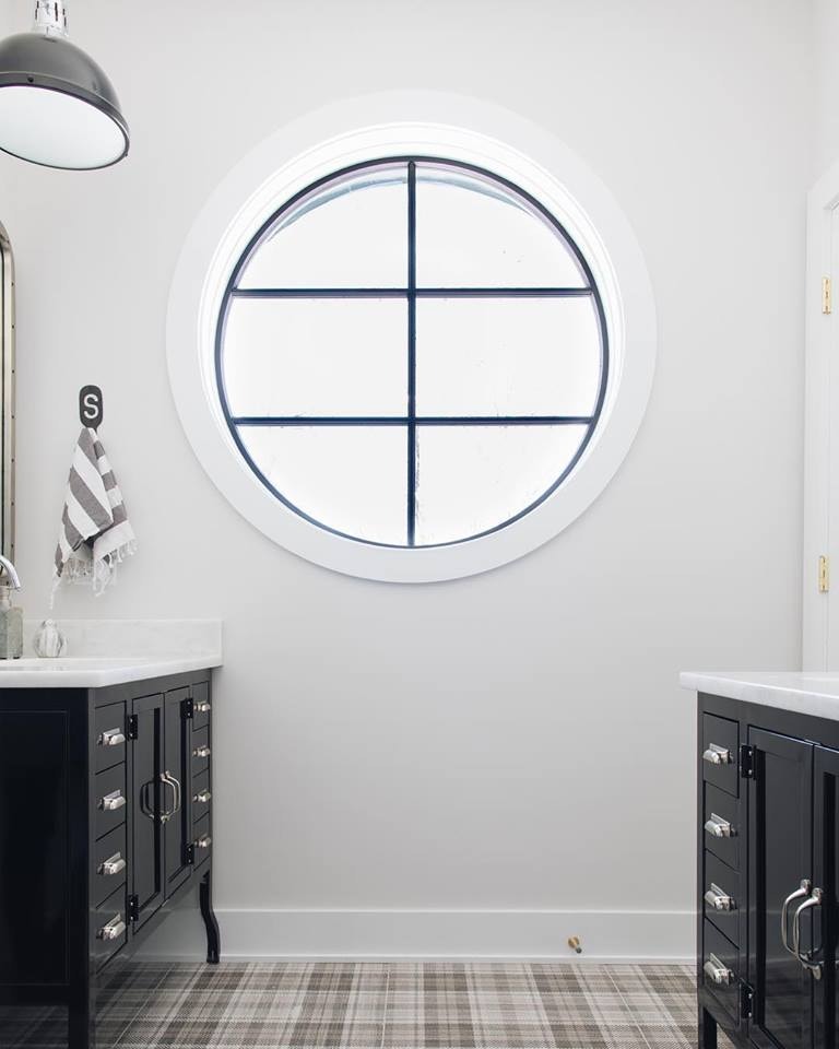 white bathroom with black vanities on either side and a large circle window in the middle