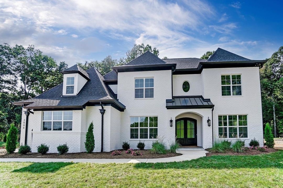 The exterior of a white brick home has white traditional windows, including an oval window above the front door.