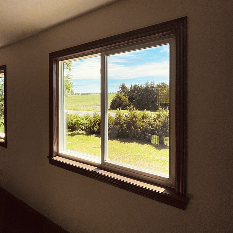 A white vinyl replacement window with black trim frames a sunny rural view in Peck, KS.