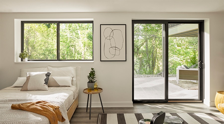Black sliding door to the right of a black sliding window that is over a natural-colored bed.