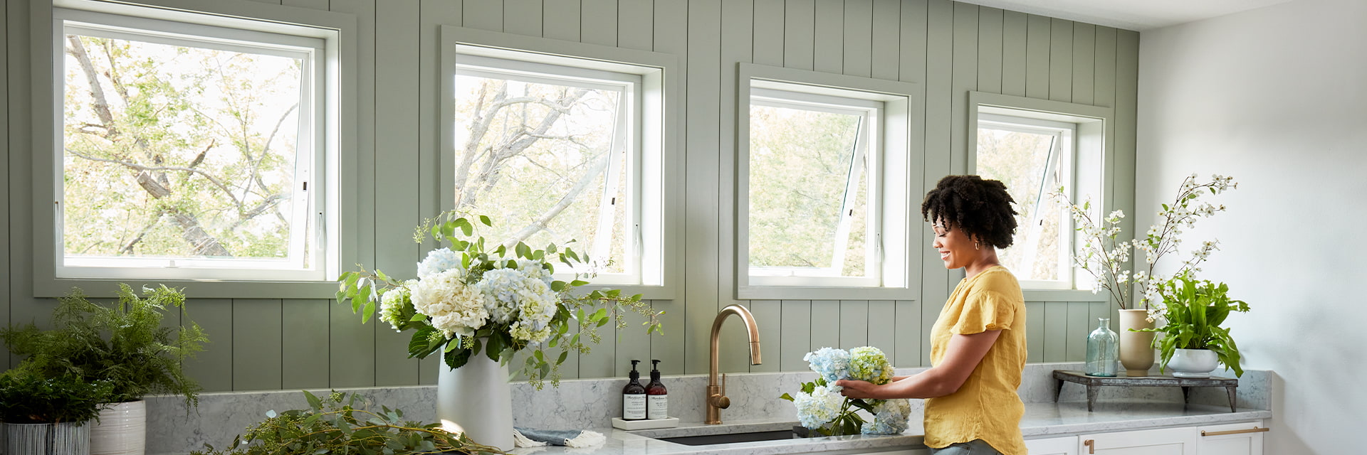 four square awning windows over a long cupboard where a woman is arranging flowers