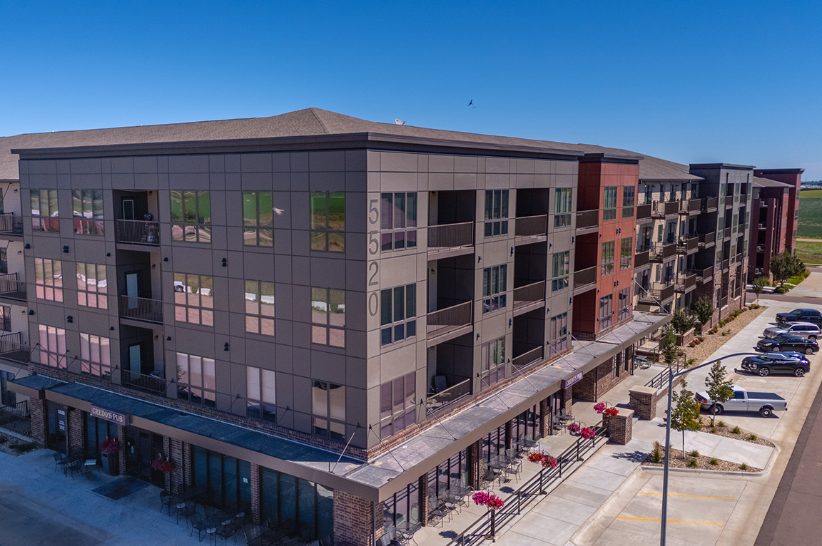 A modern apartment building with large apartment windows and balconies overlooking a parking lot.
