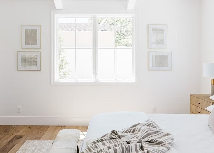 two white casement windows on the other side of a bed in this all-white master bedroom