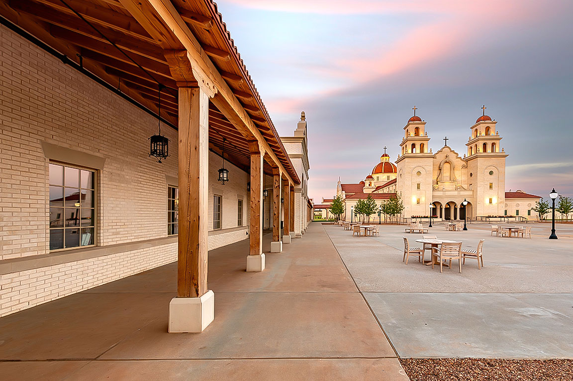 Open courtyard with wooden covered walkway and church building in background at sunset