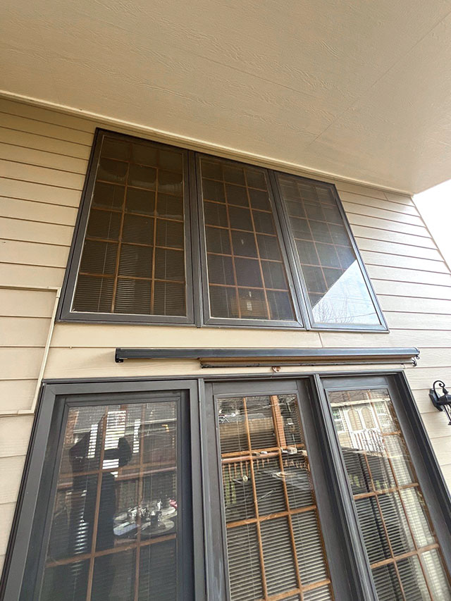 Before image showing a house exterior with gray-framed windows, highlighting the need for replacement windows.