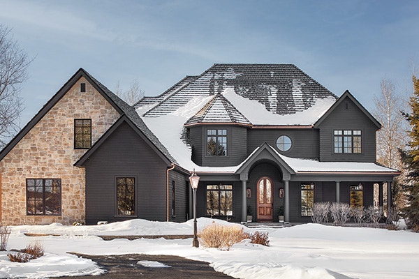 exterior of a large black and brick home with snow on the roof