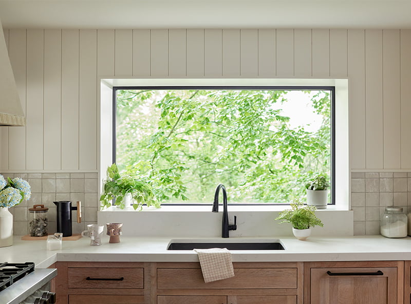 Farmhouse-style kitchen sink with several green plants and a beautiful, sound-resistant window