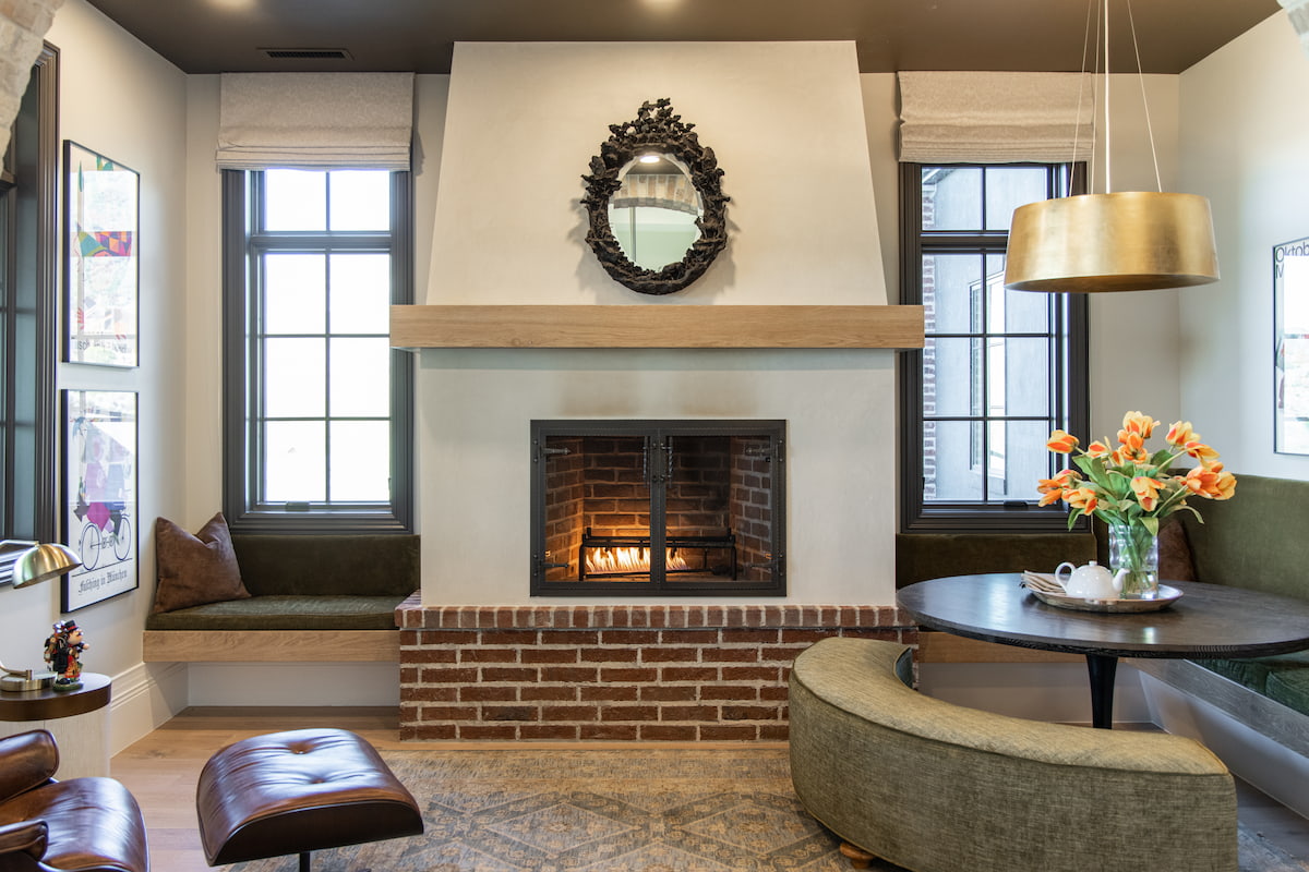A cozy parlor room features a fireplace with casement windows on each side and bench seating below.
