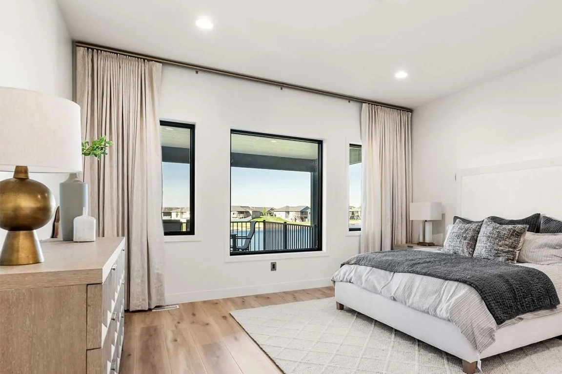 Bright modern primary bedroom with large windows, neutral decor, and wood flooring.