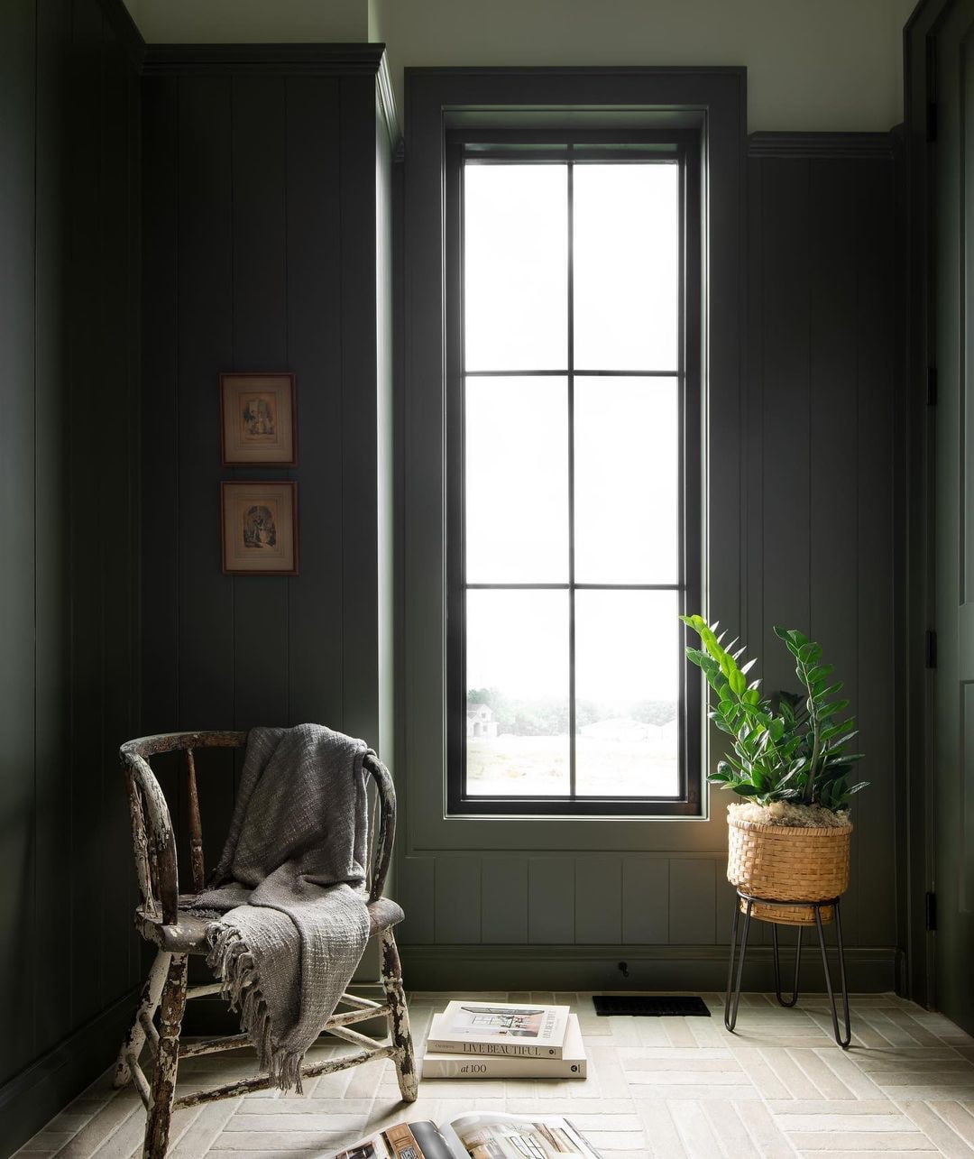 At the end of a hallway is a moody sitting area with a chair, books and a picture window.