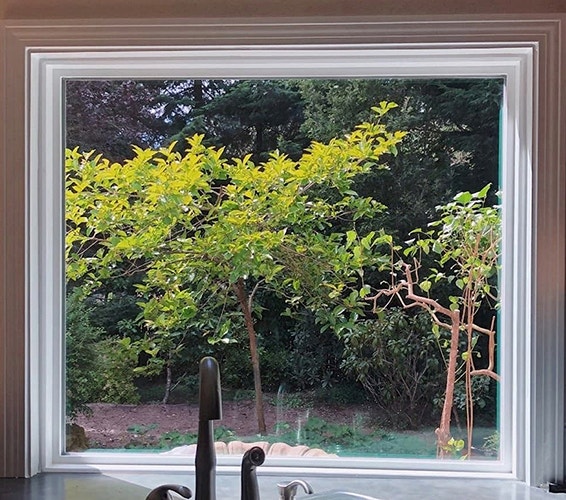 A large, white picture window behind a kitchen faucet, bringing a view of the trees outside 