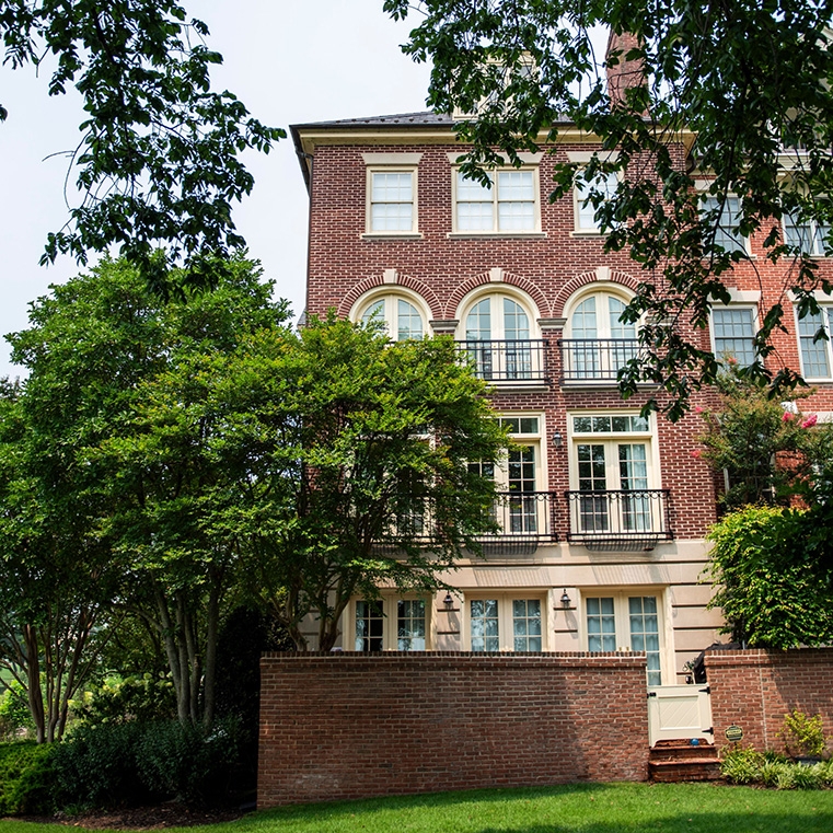 Cream French doors and windows on back of traditional home in Alexandria with large green trees.