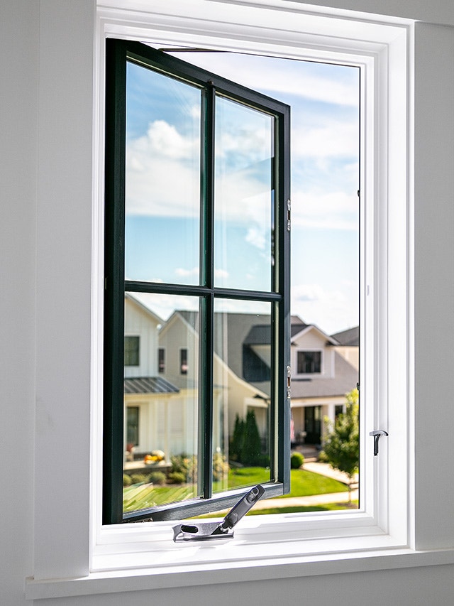A black frame bow window open, showcasing a view of a neighborhood with houses and blue sky.