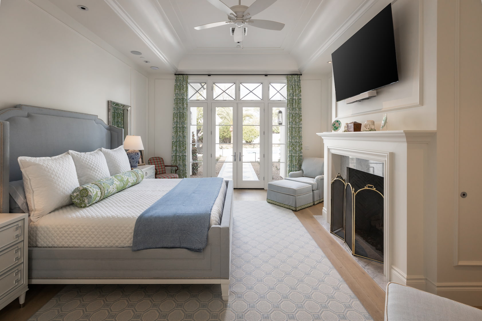 A sophisticated bedroom features a large bed, fireplace and custom French doors leading to the backyard.