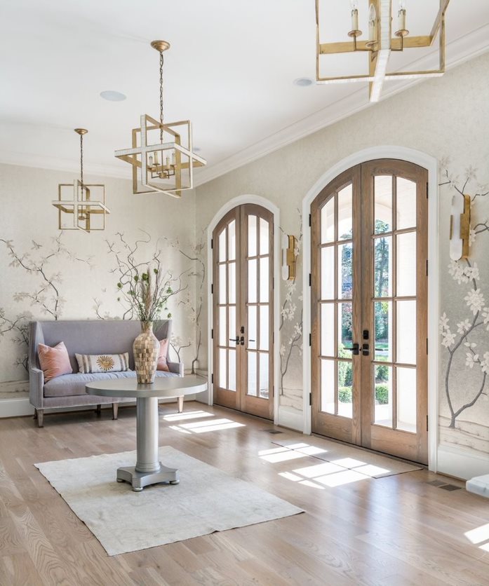 Arched French doors in a light wood stain connect an indoor living room space to an outdoor patio.