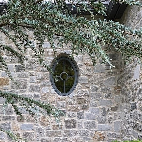 A custom oval window on a stone home with fir trees on the exterior