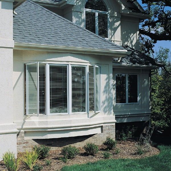 Exterior of home with a white bow window with casement windows and blinds