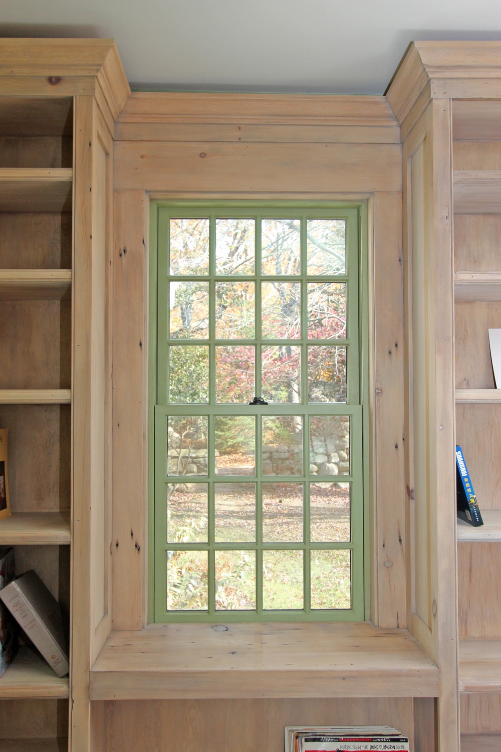 green double-hung window surrounded by natural wood bookcase on either side