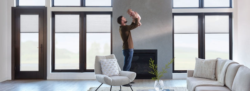 dad and baby in a living room in front of a wall of windows and hinged door