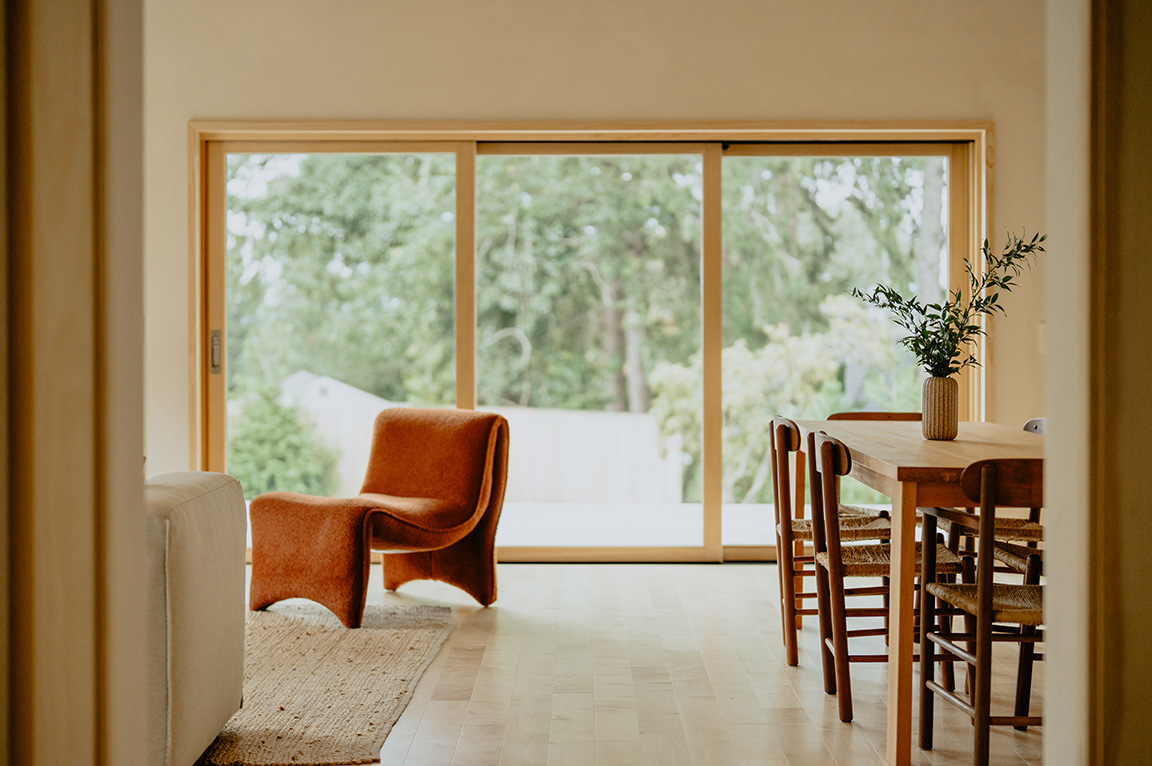 Large energy efficient windows with wooden frames overlook a backyard from a cozy dining area.