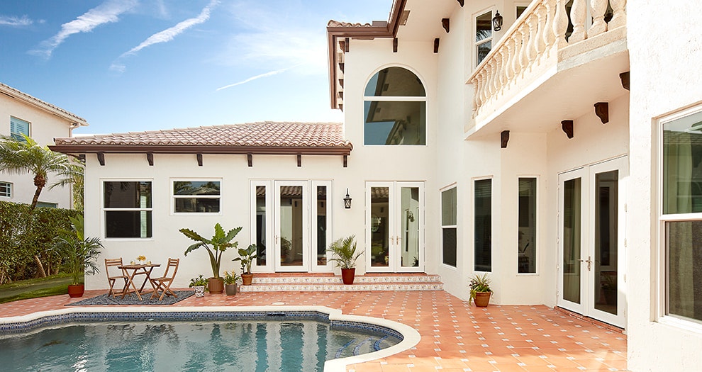 Spanish-style home's courtyard with a custom pool and coastal windows and patio doors.
