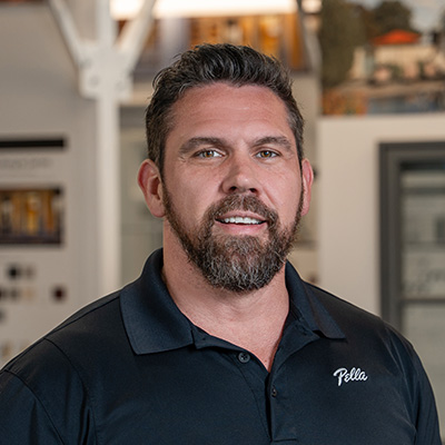 A man with a beard and mustache is wearing a black Pella shirt