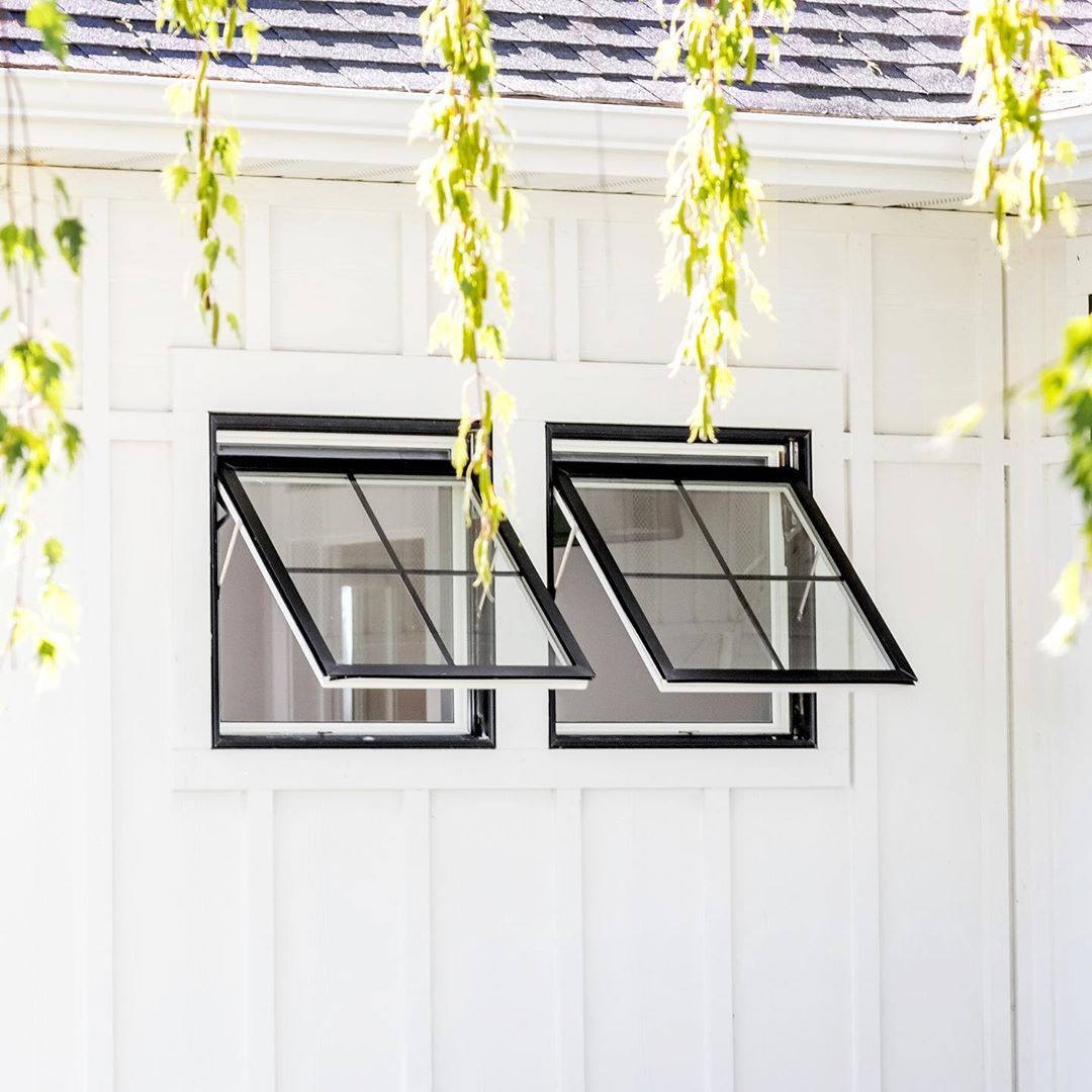 white siding with two black awning windows open and tree limbs hanging down