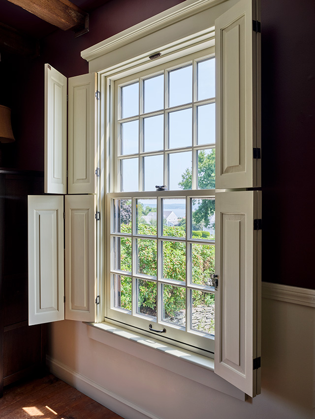 An interior view of white traditional windows with open shutters, showcasing a scenic outdoor view. 