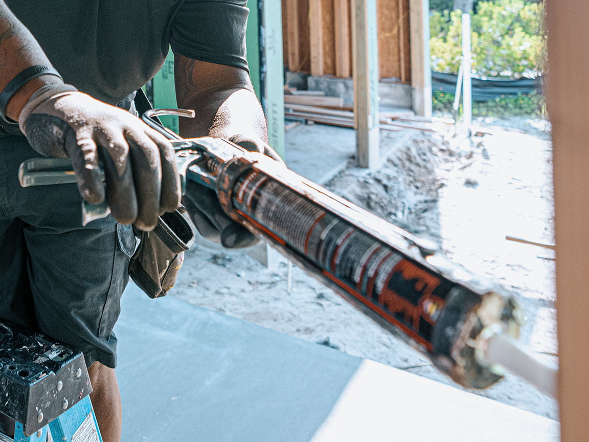 A man is standing in the snow using sealant on a window on the exterior of the frame.