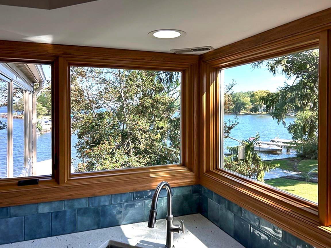 Scenic view of a lake seen through corner windows in a kitchen with wooden frames, blue tiles on the counter, and a modern faucet.