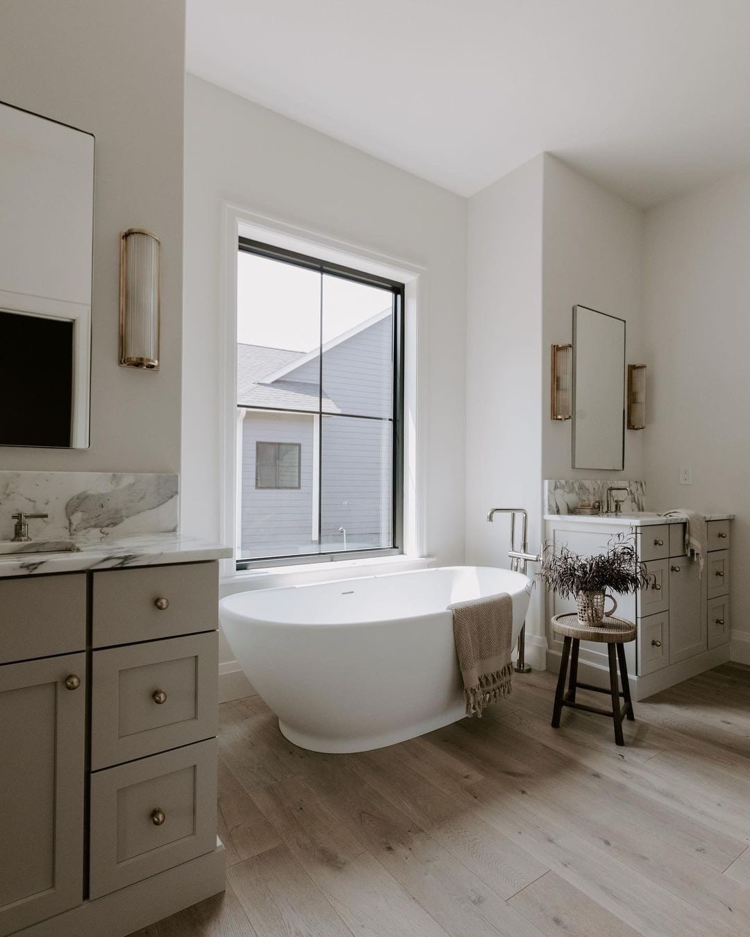 Between two vanities sits a white bathtub with a black picture window behind it.