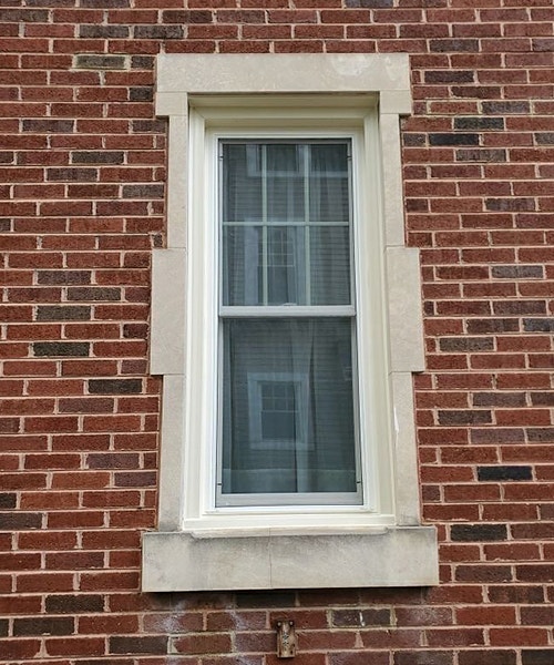 a single white window with stone trim on a brick home