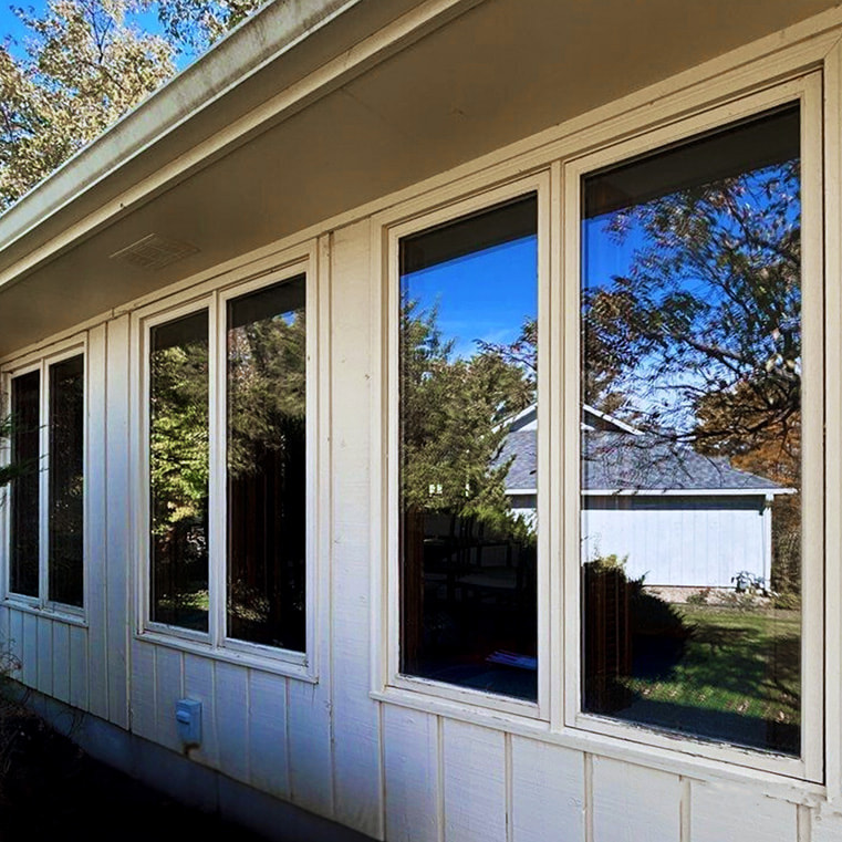 Sunroom windows with yellow siding, showcasing a modern design and surrounding greenery.